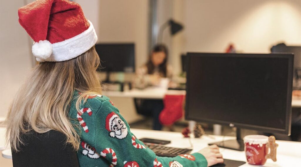 Chica trabajando en la oficina con gorro de Papa Noel y jersey navideño