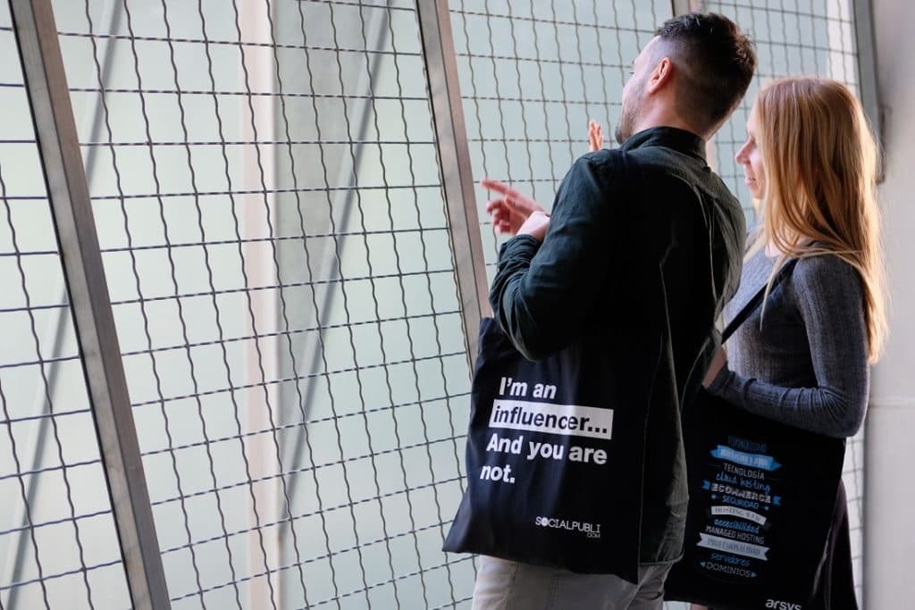 Dos personas haciendo un comentario llevando bolsas corporativas